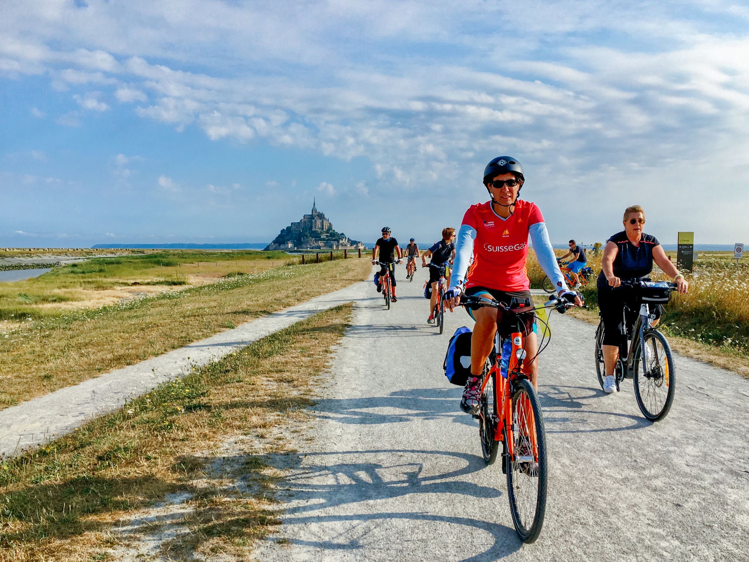 Ciclisti durante una vacanza in bici che pedalano lungo la ciclabile con Mont-Saint-Michel sullo sfondo
